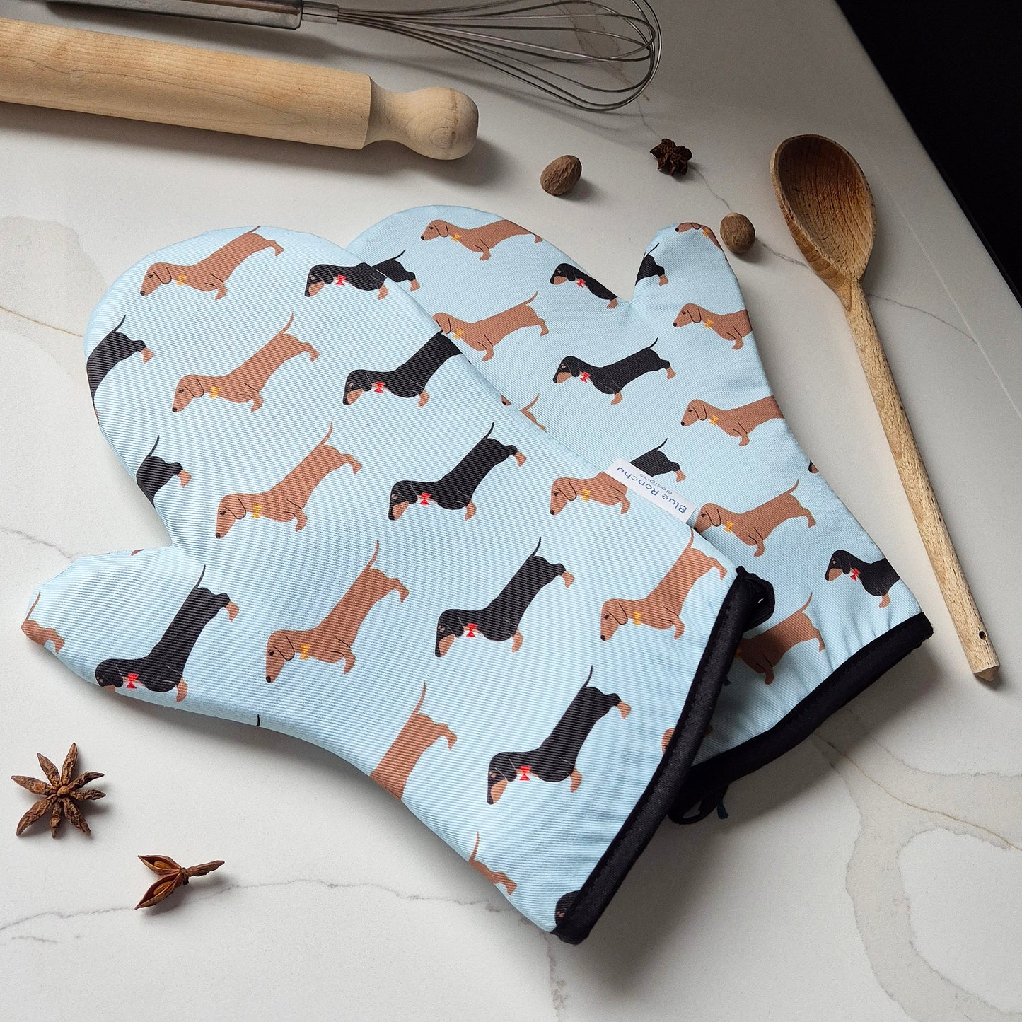 Oven mitts with dachshund pattern on a kitchen counter with cooking utensils.