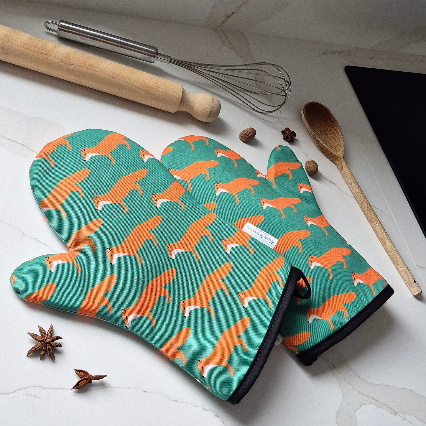 Oven mitts with fox pattern on a kitchen counter with utensils