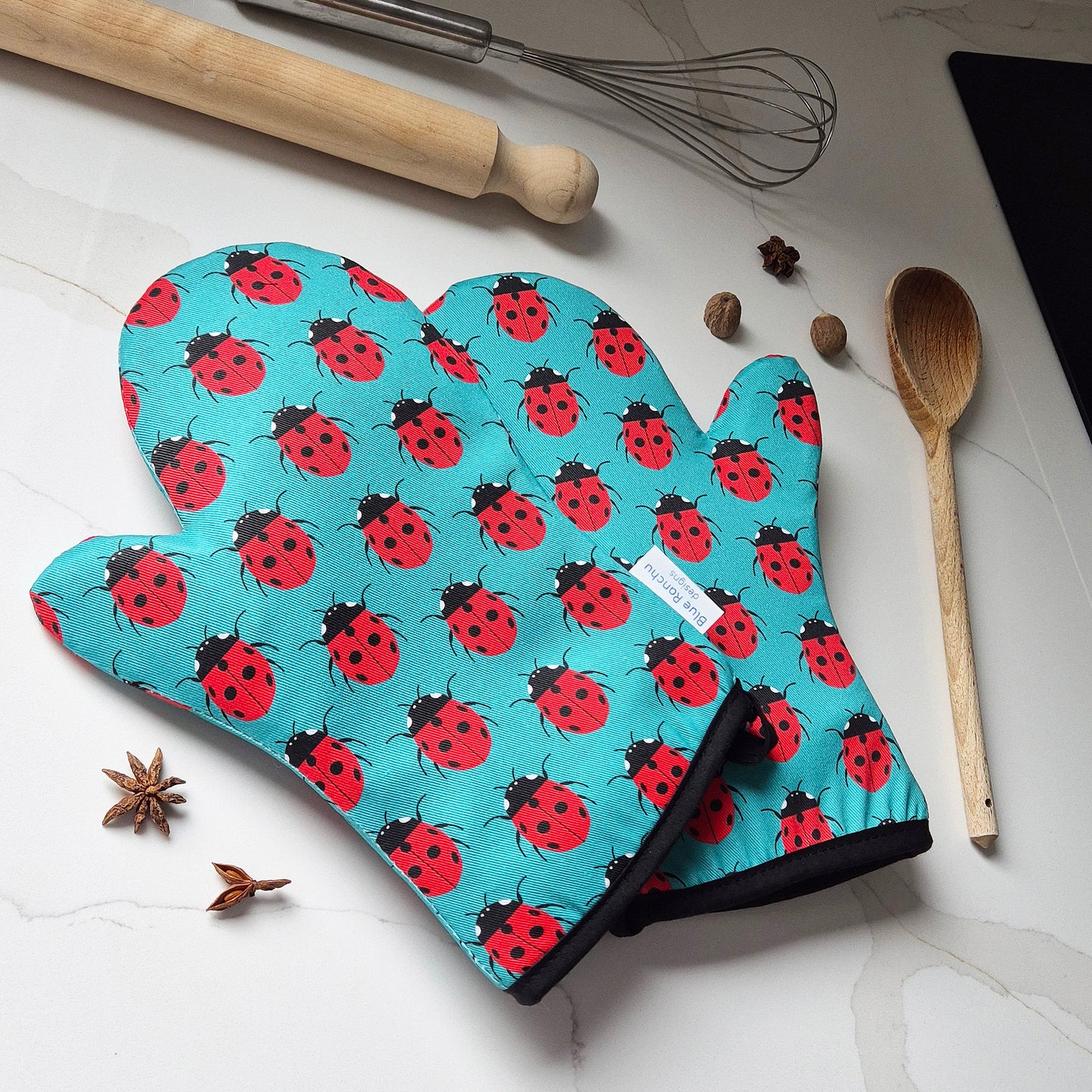 Oven mitts with ladybird pattern on a kitchen counter with utensils and spices.