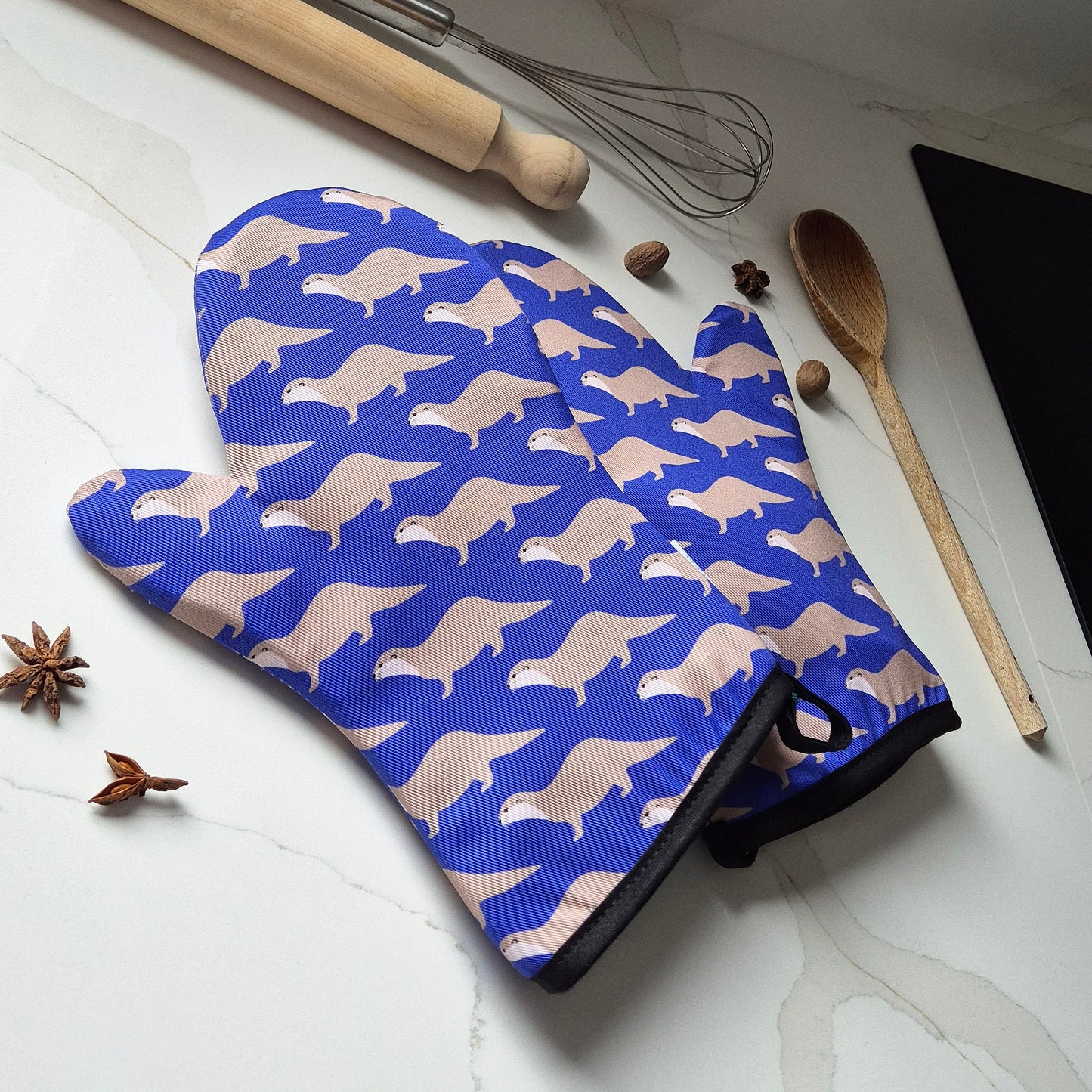 Oven mitts with otter pattern on a kitchen counter with utensils