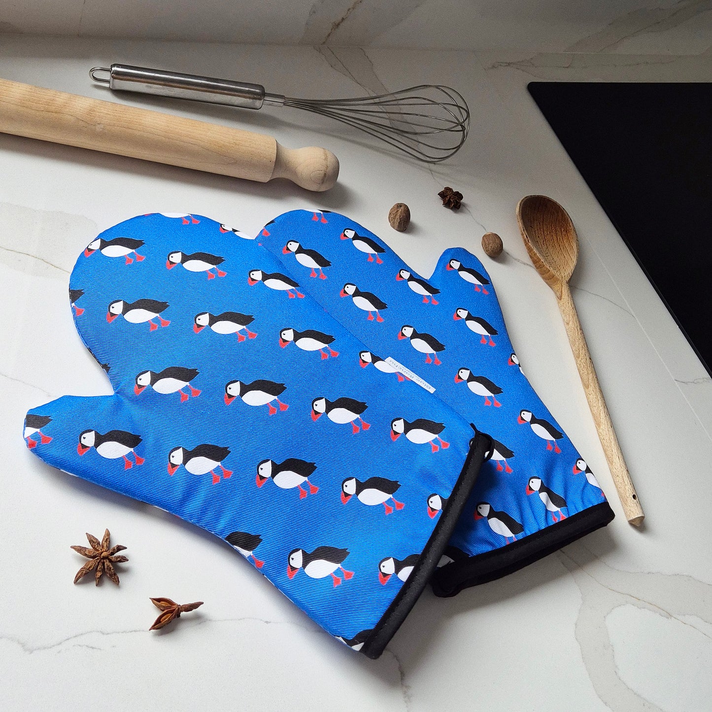 Blue oven mitt with puffin pattern on a kitchen counter with cooking utensils.