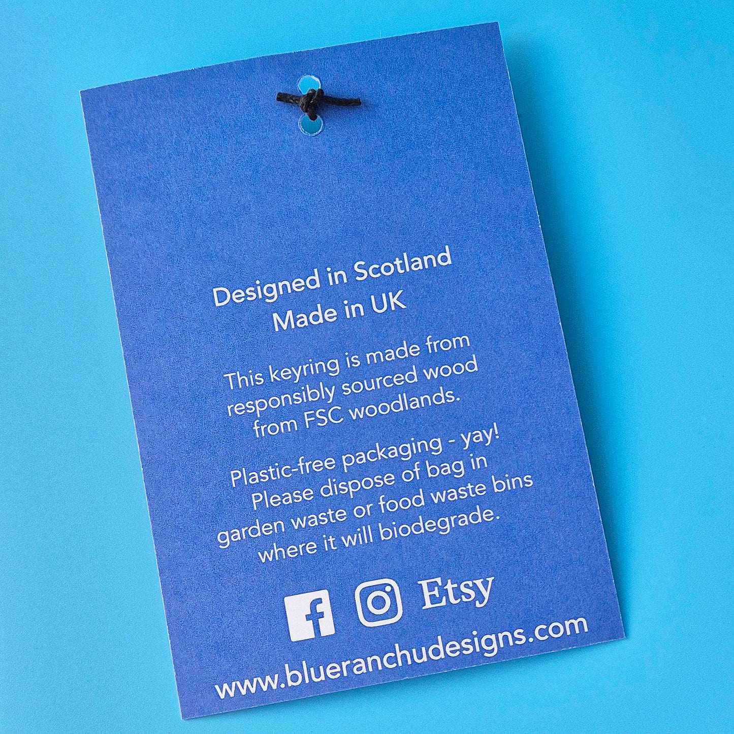 Blue keyring packaging with text about design location, material sourcing, and disposal on a blue background.