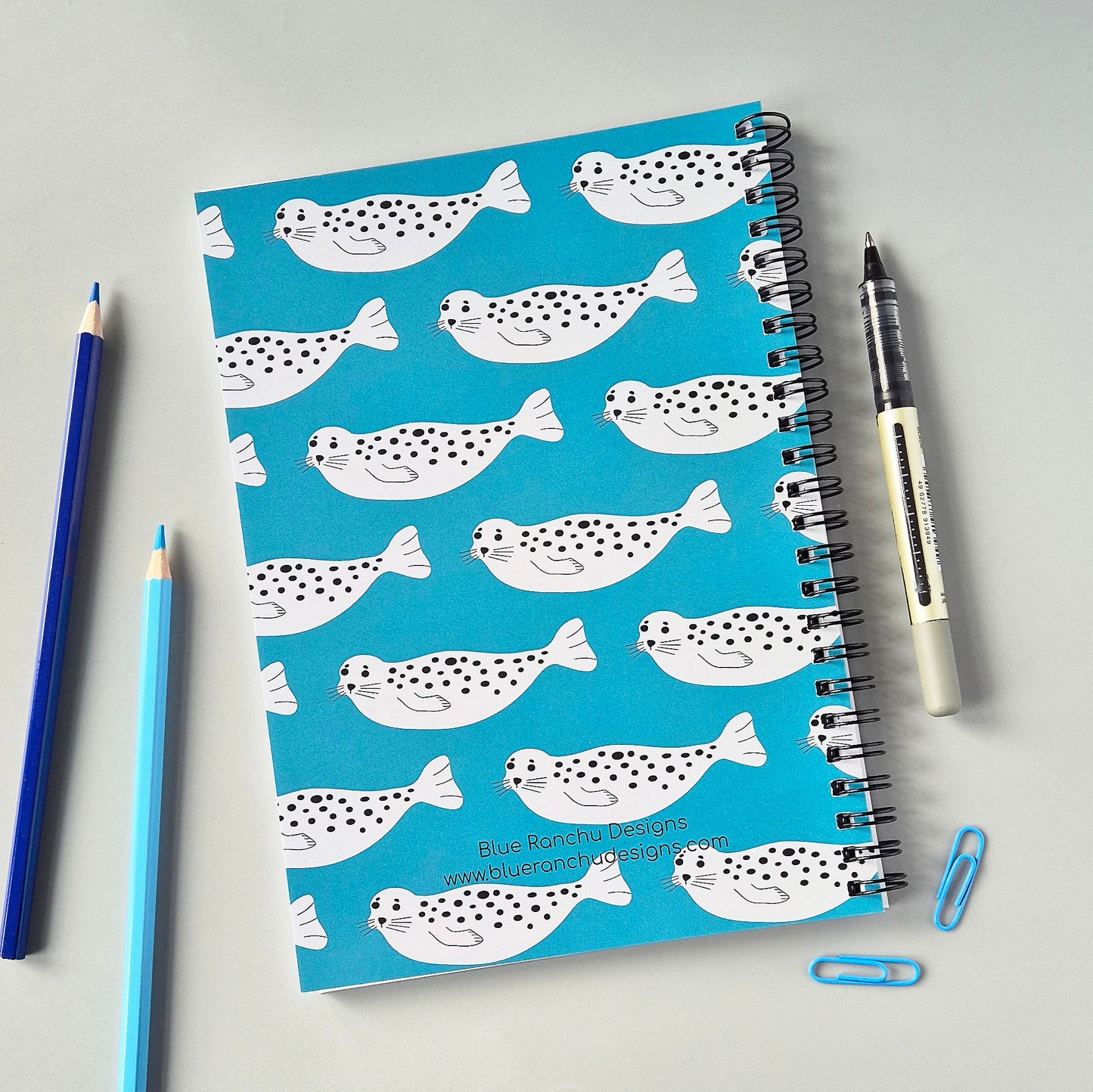 A5 wirebound notebook with a repeating Seal design on a turquoise background