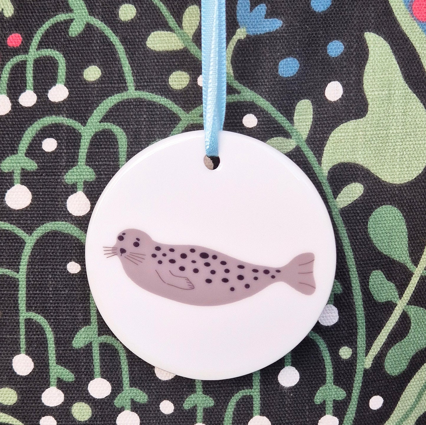 Round ceramic hanging decoration with a Harbour Seal design and a blue ribbon