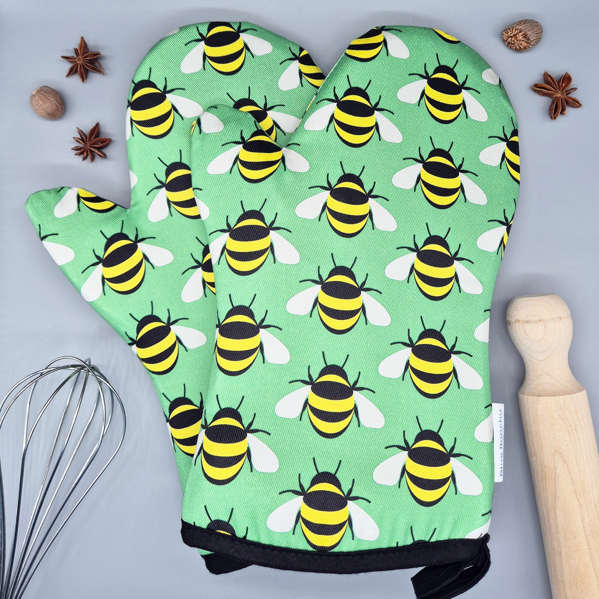 Oven mitts with bee pattern on a gray surface with kitchen items.