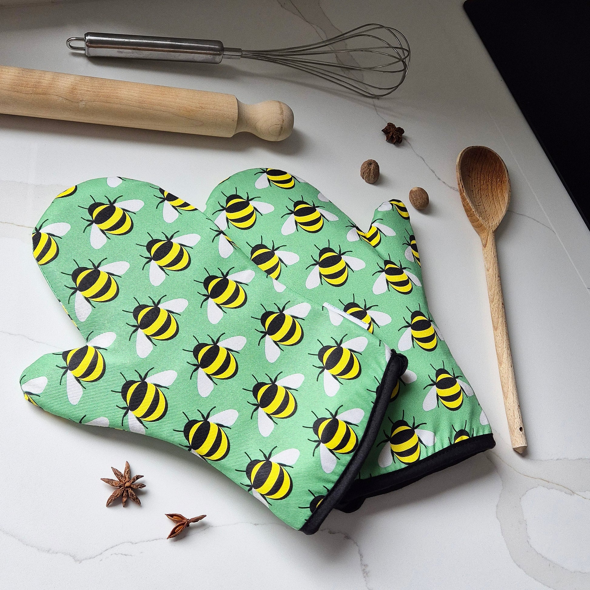 Oven mitt with bee pattern on a kitchen counter with utensils and spices.