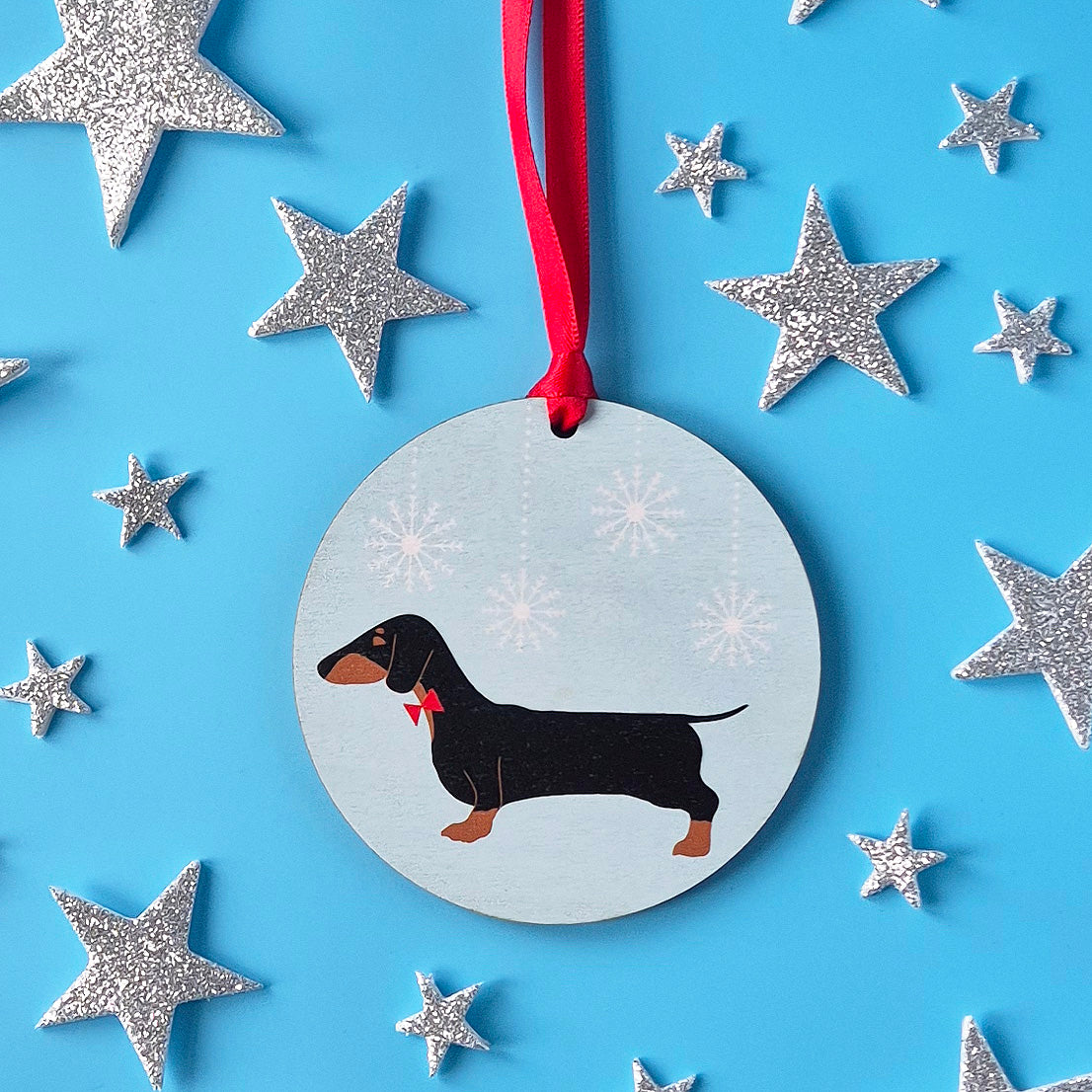 Decorative round decoration with a dachshund illustration on a blue background with silver stars.