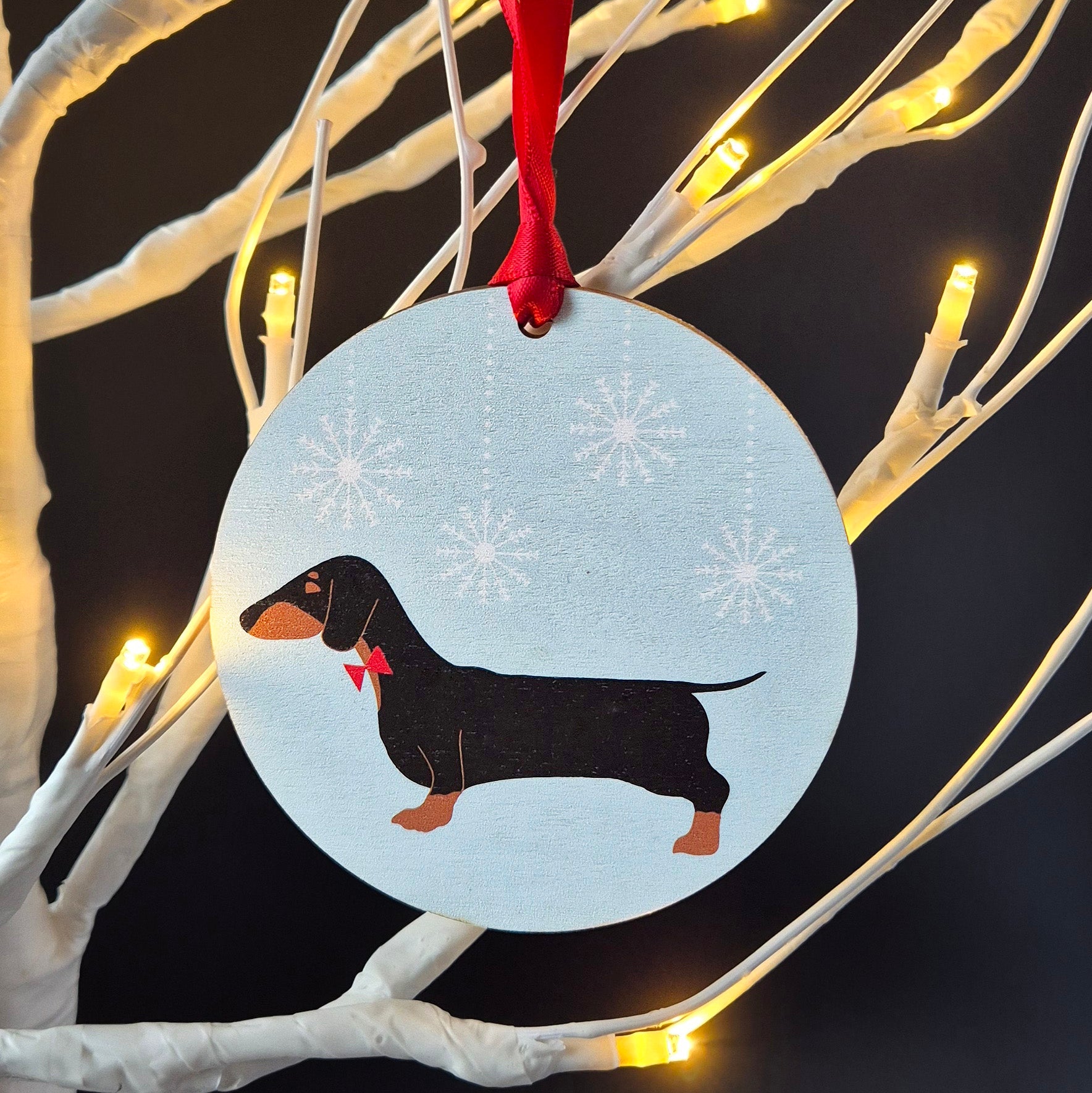 Black and Tan Dachshund design on a pale green snowy background on a round wooden Christmas decoration