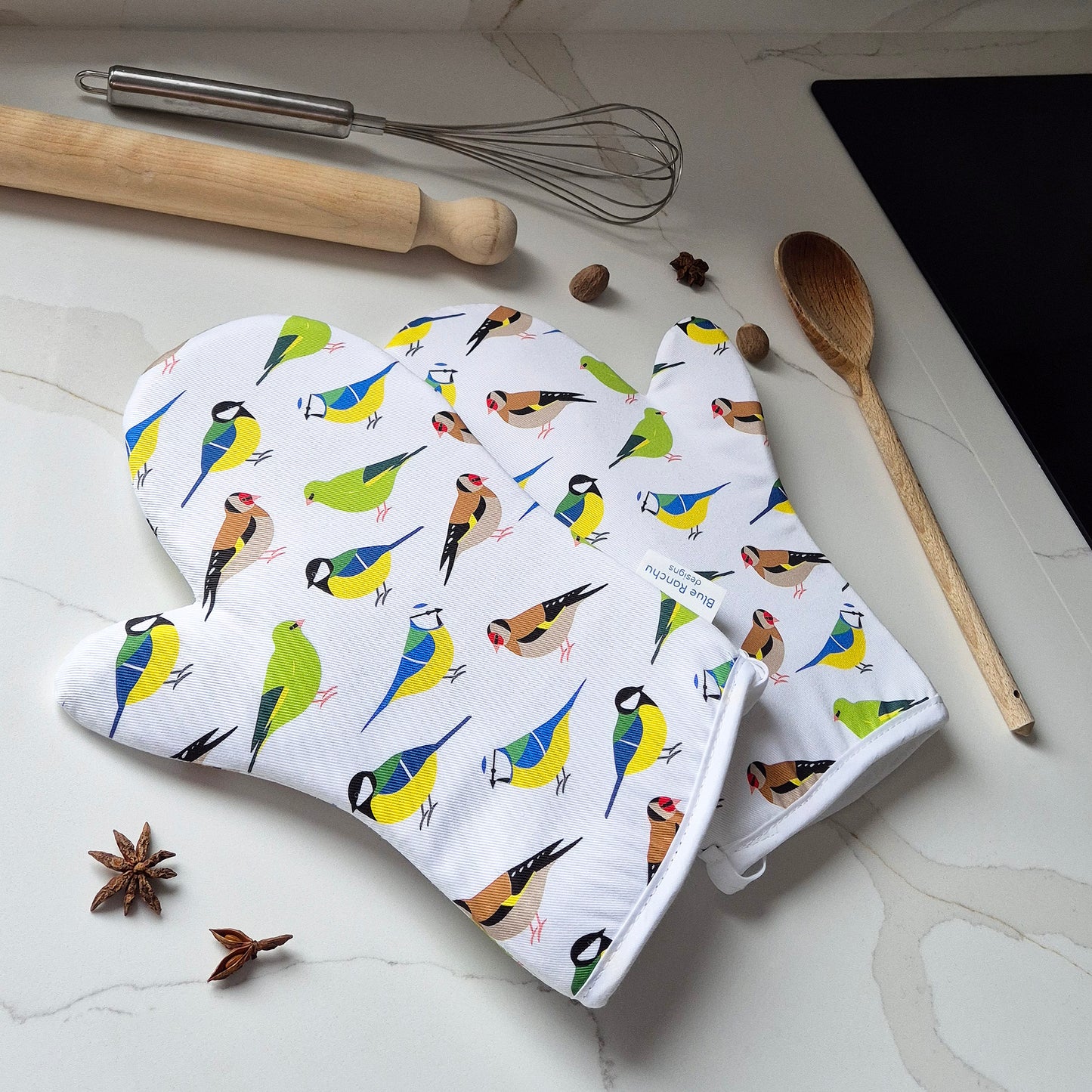 Oven mitts with garden bird pattern on a kitchen counter with cooking utensils.