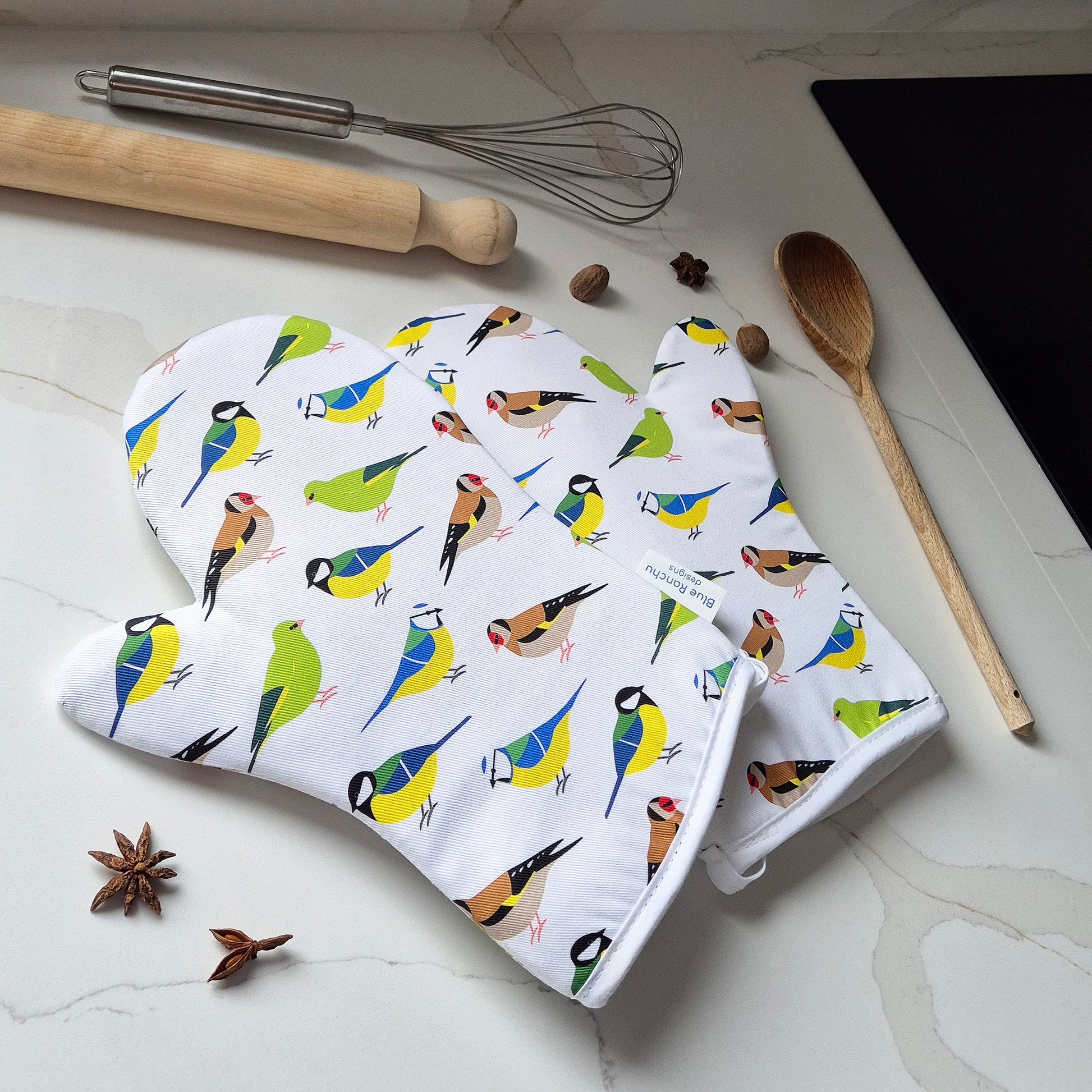 Oven mitts with garden bird pattern on a kitchen counter with cooking utensils.
