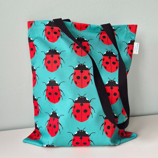 Tote bag with Ladybird repeat design on a turquoise background with black handles