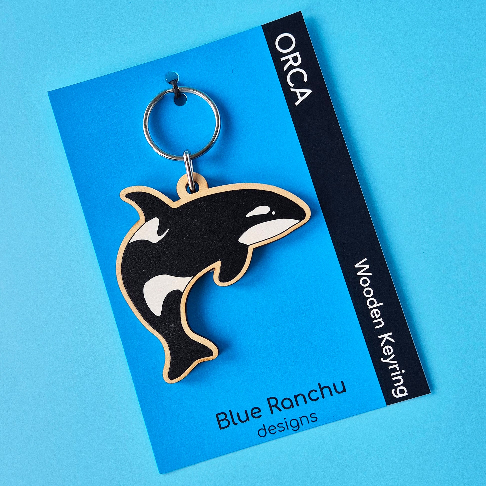 Orca shaped wooden keyring on a blue backing card