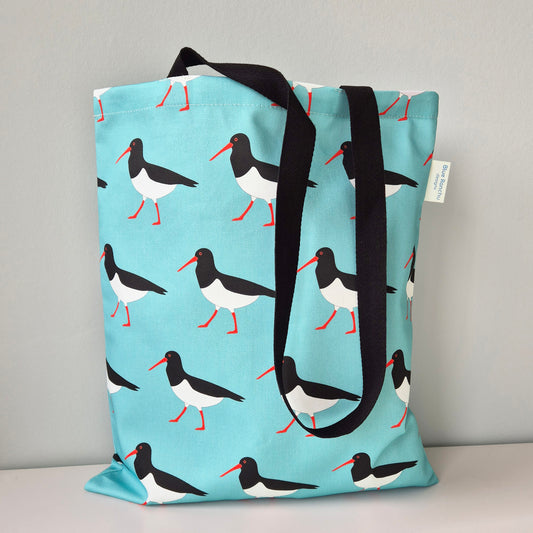 Tote bag with an Oystercatcher pattern and black handles on a turquoise background