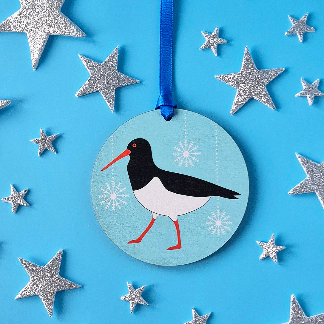Decorative wooden ornament with an Oystercatcher design on a blue background with silver stars