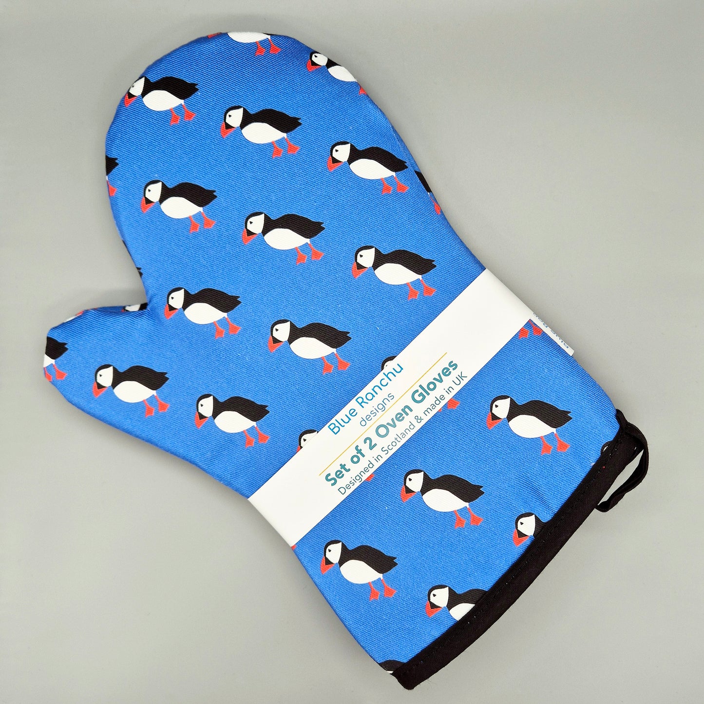Blue oven glove with puffin pattern on a gray background