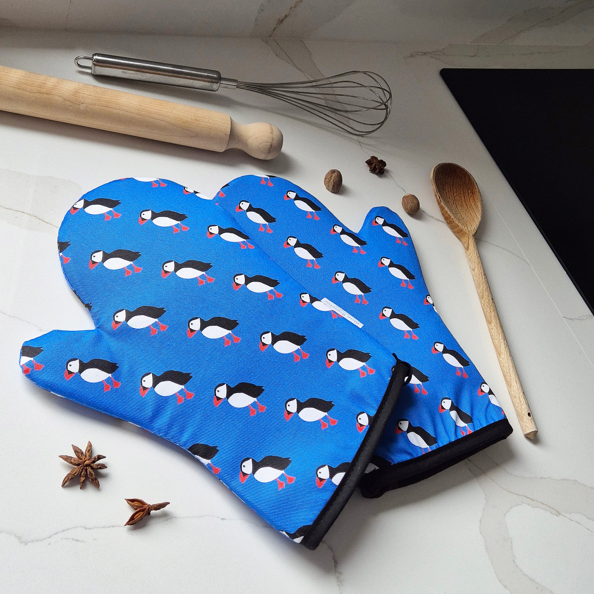 Blue oven mitt with puffin pattern on a kitchen counter with cooking utensils.