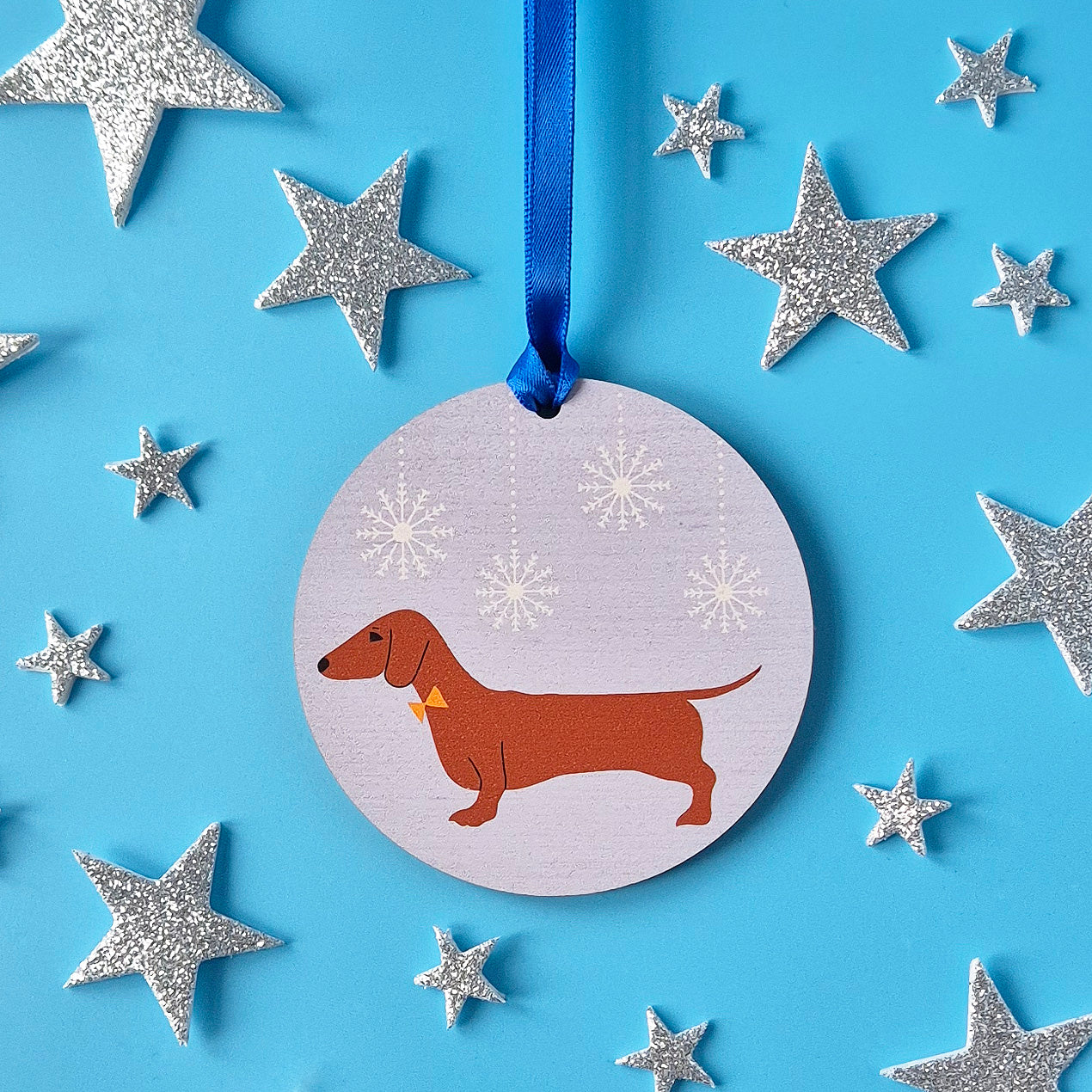 Decorative wooden ornament with a red dachshund design surrounded by silver stars on a blue background