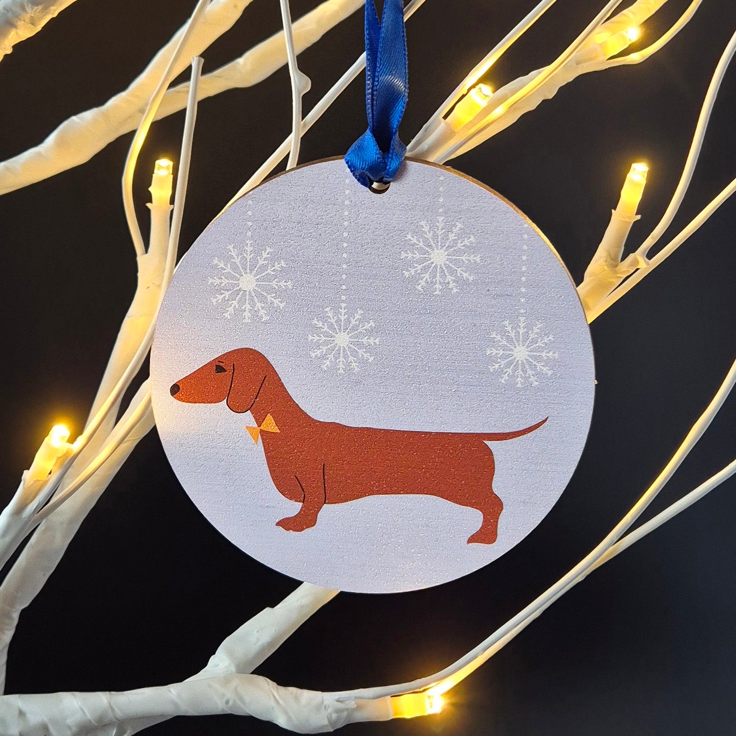 Red Dachshund on a blue snowy background design on a round wooden Christmas decoration