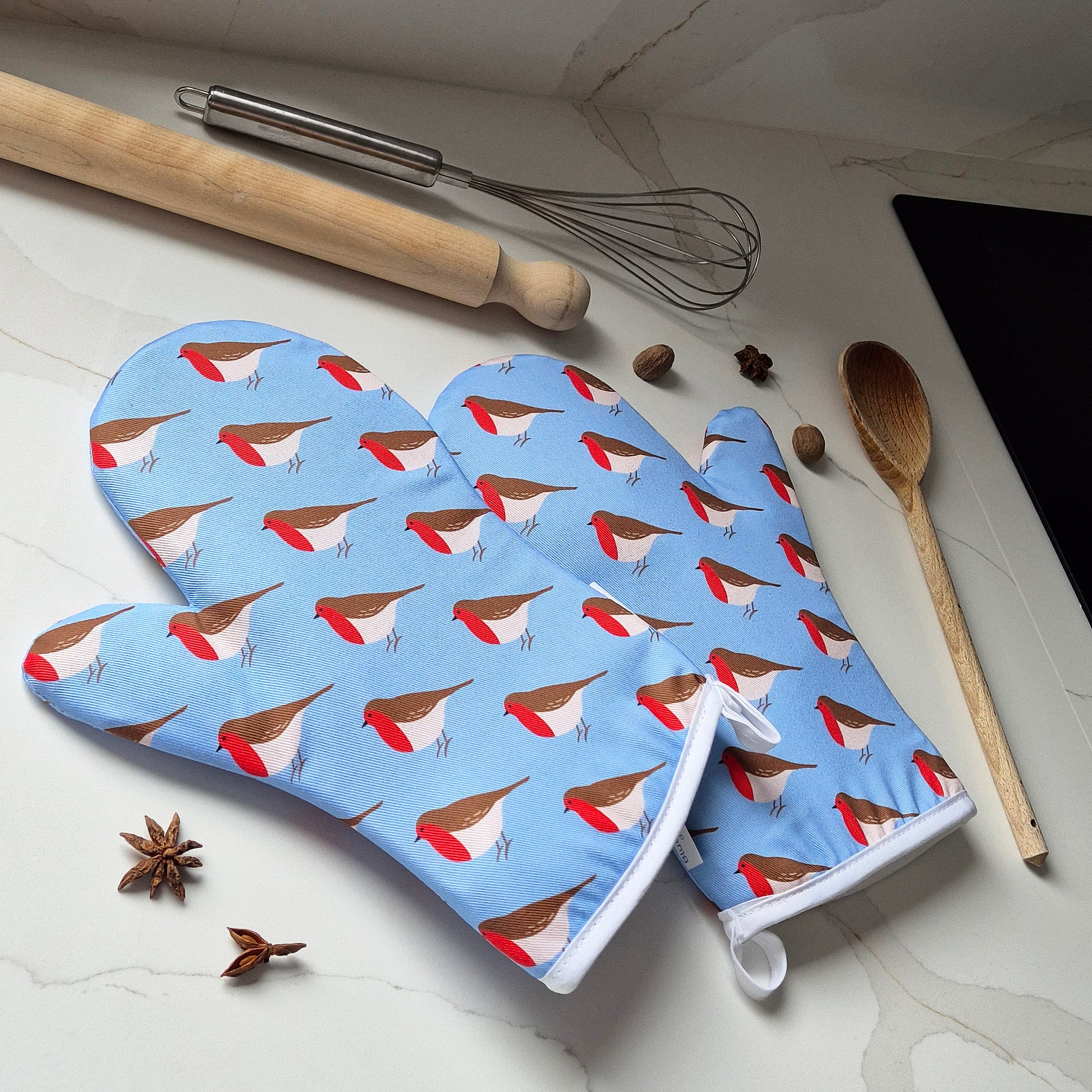 Oven mitts with Robin pattern on a kitchen counter with utensils.