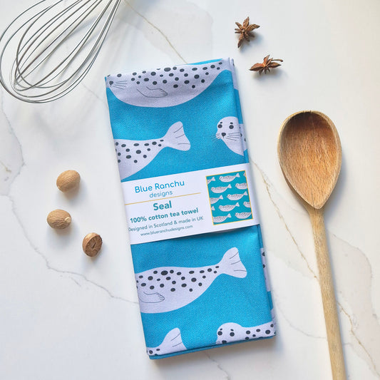 Grey spotted seals on a turquoise background folded cotton tea towel with belly band