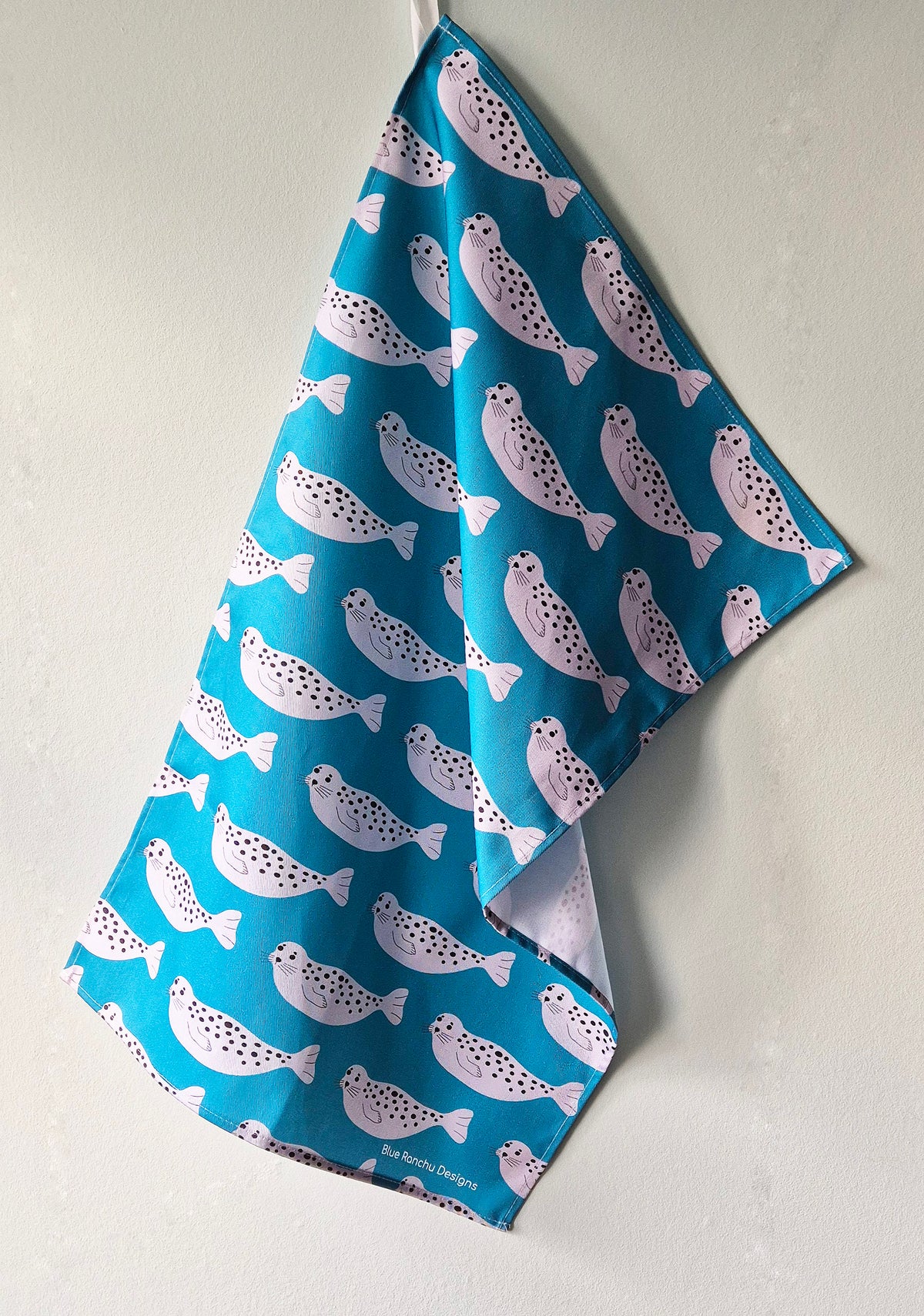 Repeating Seal pattern on a turquoise background, cotton tea towel