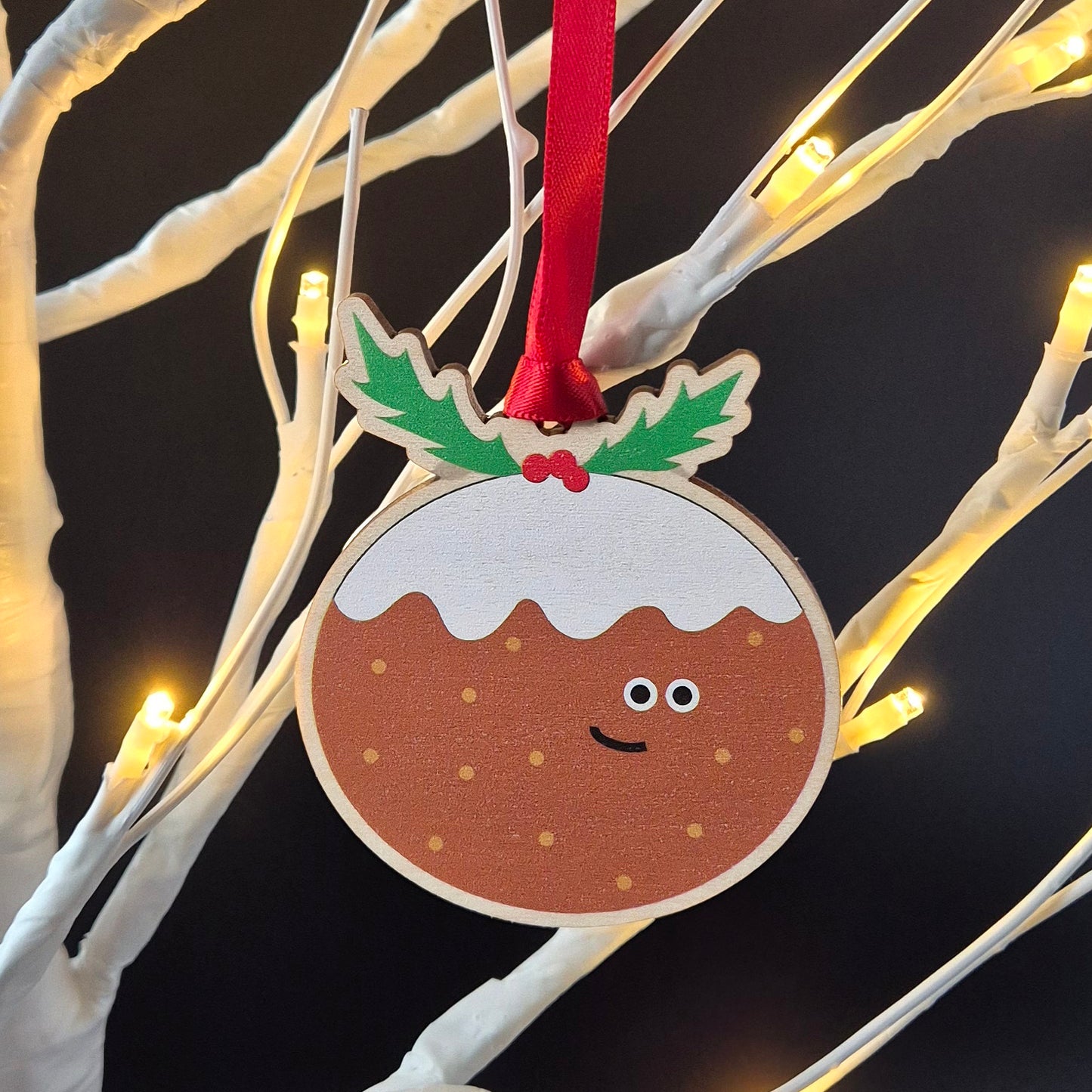 Smiling Christmas pudding wooden decoration hanging from a Christmas tree