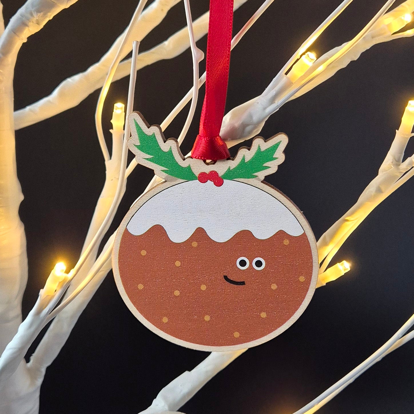 Smiling Christmas pudding wooden decoration hanging from a Christmas tree